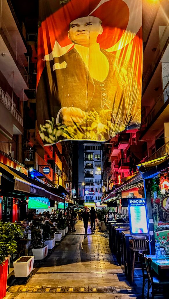 a banner of Atatürk hanging above an alley of bars and restaurants in Izmir, Turkiye